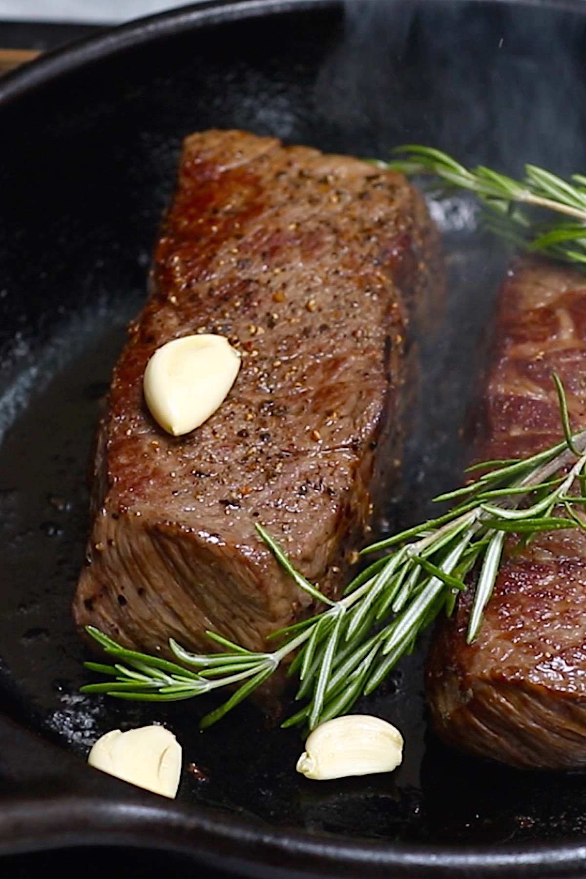 Chuck steak searing in a cast iron pan with fresh rosemary and garlic