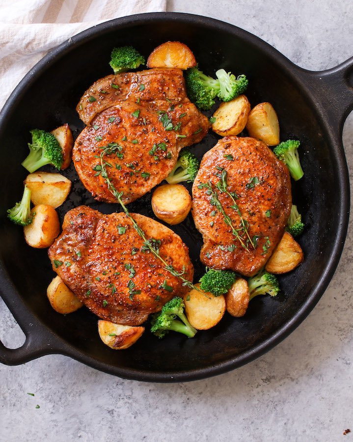 Pan fried boneless pork chops in a cast iron skillet with sauteed potatoes and broccoli and garnished with fresh thyme