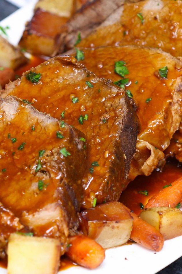 Closeup of thick slices of roast beef with gravy on top and vegetables on the side