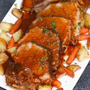 Eye of round roast on a serving platter with potatoes and carrots and minced parsley for garnish