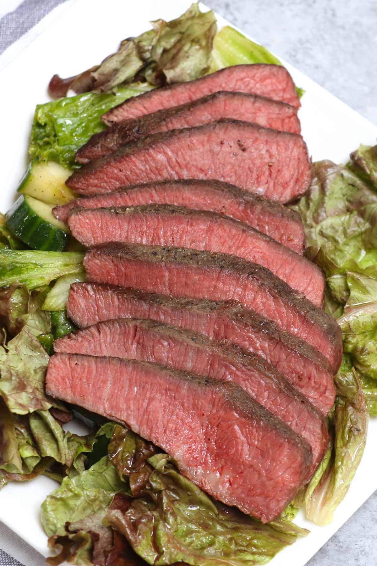 Slices of pan seared flat iron steak with a side salad