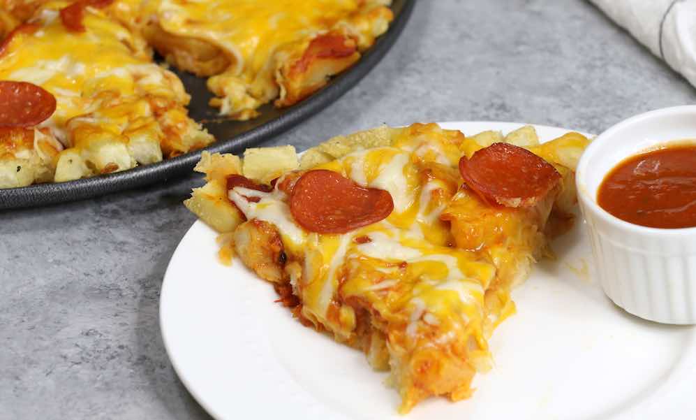 A slice of french fry pizza on a serving plate with dipping sauce