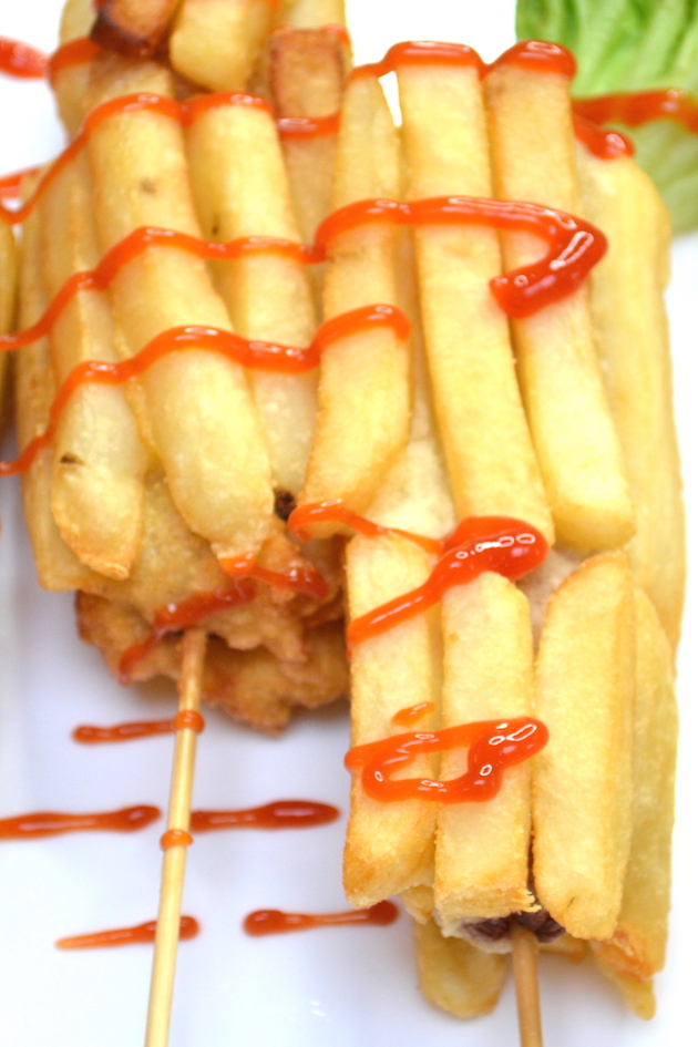 Closeup of fried hot dogs covered with french fries and dipped in ketchup