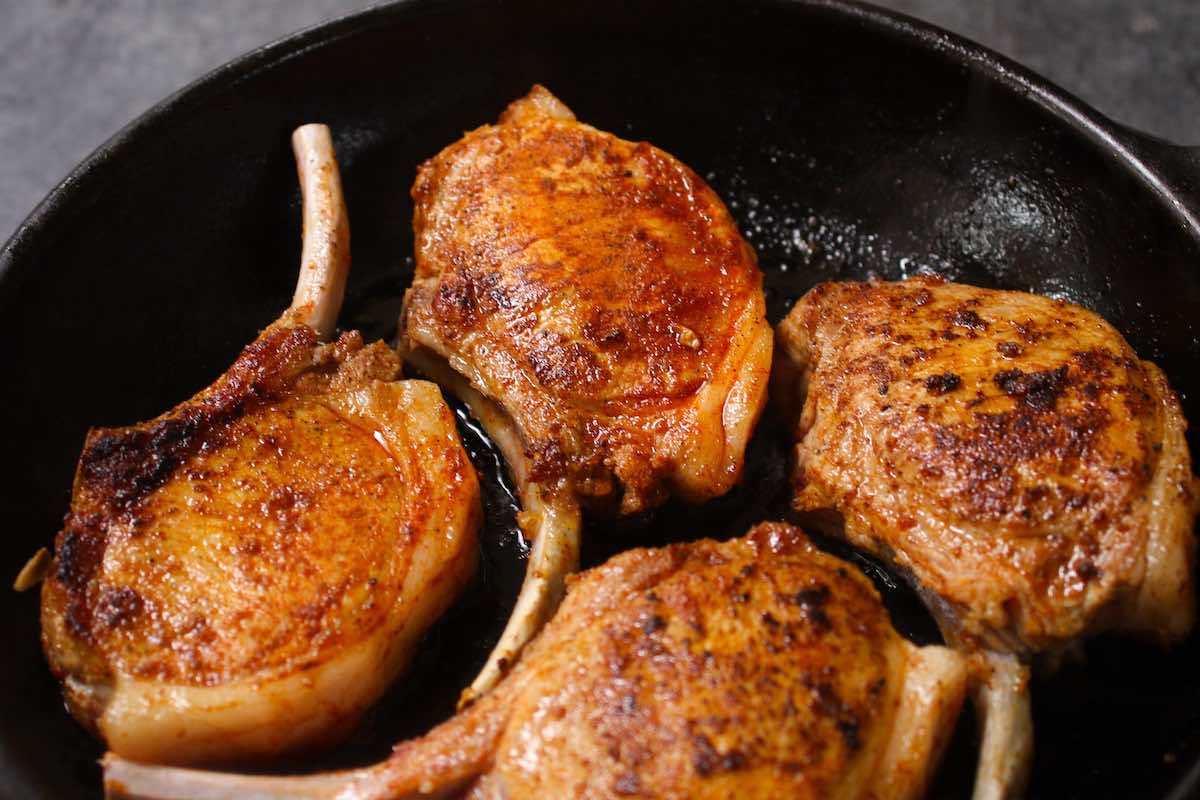 Photo showing frying pork chops in a cast iron skillet at the halfway point with a crust beginning to form on the outside