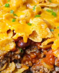 Closeup of a piece of freshly baked Frito Pie showing layers of Fritos corn ships and ground beef with chili beans, tomato sauce and melted cheddar cheese