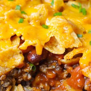 Closeup of a piece of freshly baked Frito Pie showing layers of Fritos corn ships and ground beef with chili beans, tomato sauce and melted cheddar cheese