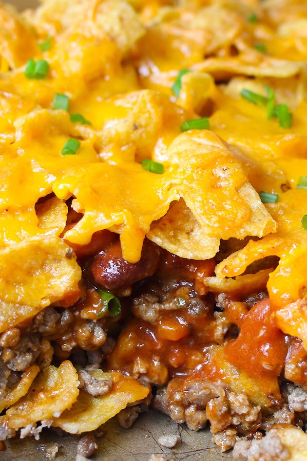 Closeup of a piece of freshly baked Frito Pie showing layers of Fritos corn ships and ground beef with chili beans, tomato sauce and melted cheddar cheese