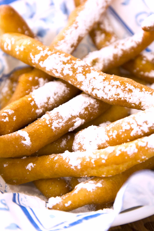 Closeup of funnel cake fries that are crispy golden on the outside and fluffy on the inside, served in a basket with a dusting of powdered sugar