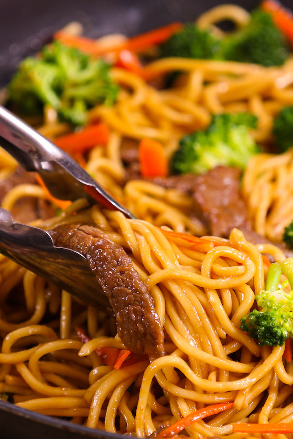 Closeup of garlic beef lo mein being served straight out of a skillet using tongs for an easy weeknight dinner idea