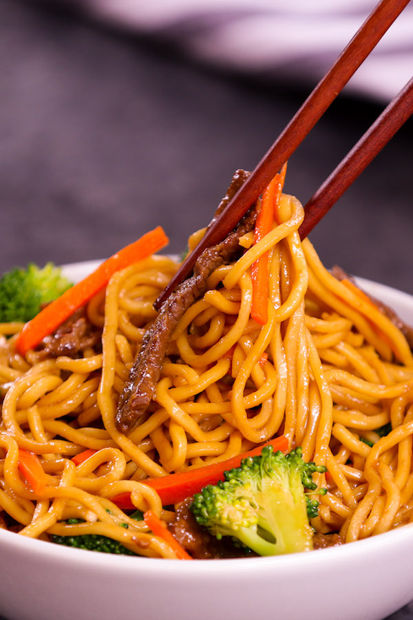 Picking up Asian noodles out of a serving bowl using chopsticks