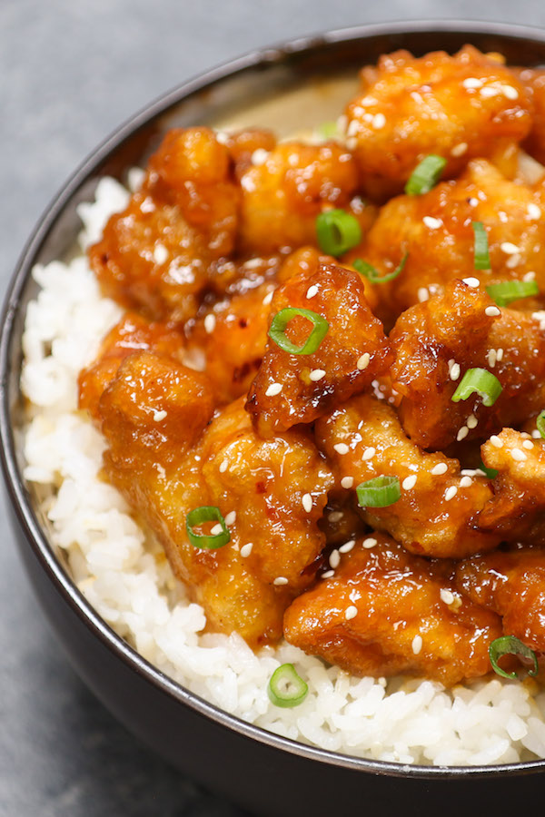 General Tso's Chicken - this photo shows a closeup of crispy chicken pieces with minced green onions and sesame seeds in a sticky sauce on top of white rice served in a bowl for a delicious weeknight dinner idea that's easy to make in 20 minutes