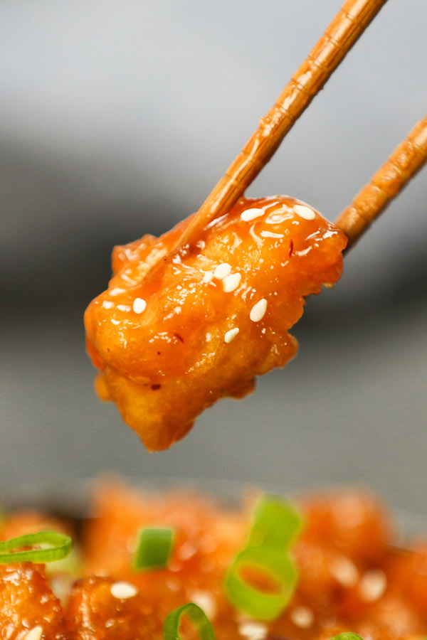 General Tso's Chicken - a closeup of a piece of General Tso Chicken held with chopsticks ready to be eaten