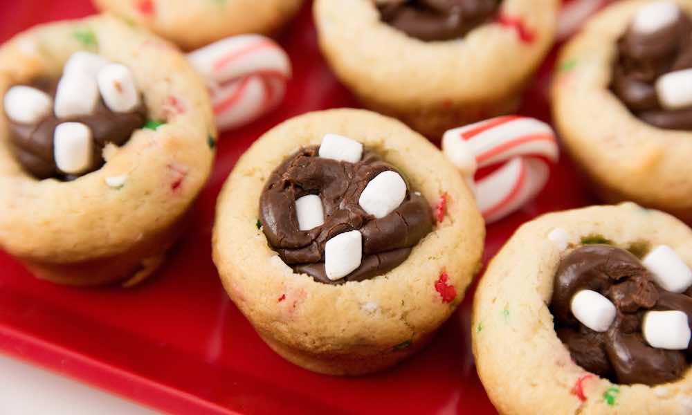 Closeup of Hot Chocolate Cookie Cups showing the sugar cookie cups, fudge filling and candy cane handles with mini marshmallows on top