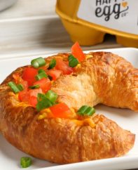 Holiday Croissant Boats are a mouthwatering breakfast recipe featuring fluffy ham and cheese omelet baked to golden perfection inside a flakey croissant and then topped with minced tomatoes and green onion for a colorful red and green holiday theme