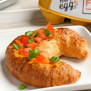 Holiday Croissant Boats are a mouthwatering breakfast recipe featuring fluffy ham and cheese omelet baked to golden perfection inside a flakey croissant and then topped with minced tomatoes and green onion for a colorful red and green holiday theme