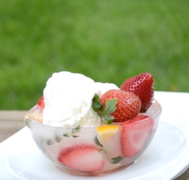 A serving of vanilla ice cream and strawberries in a decorative ice bowl