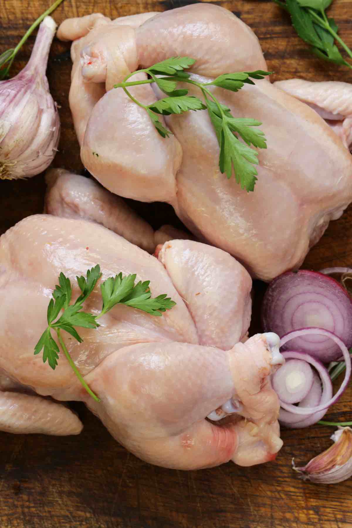 Raw whole chickens with sliced onions, garlic and parsley