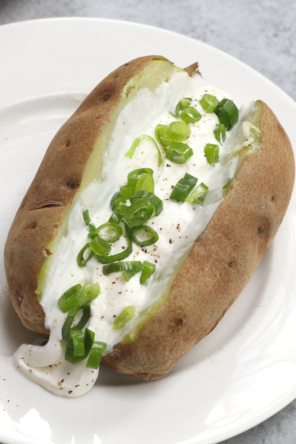 A soft and tender microwave baked potato garnished with butter, sour cream and green onions