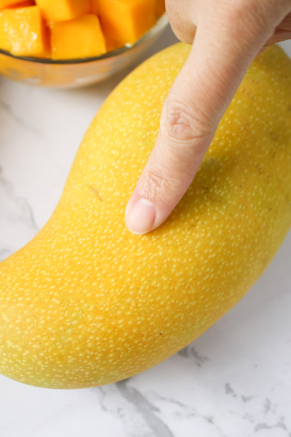 How to tell when a mango is ripe by squeezing or pressing with your hand. It should give a little when ripe.