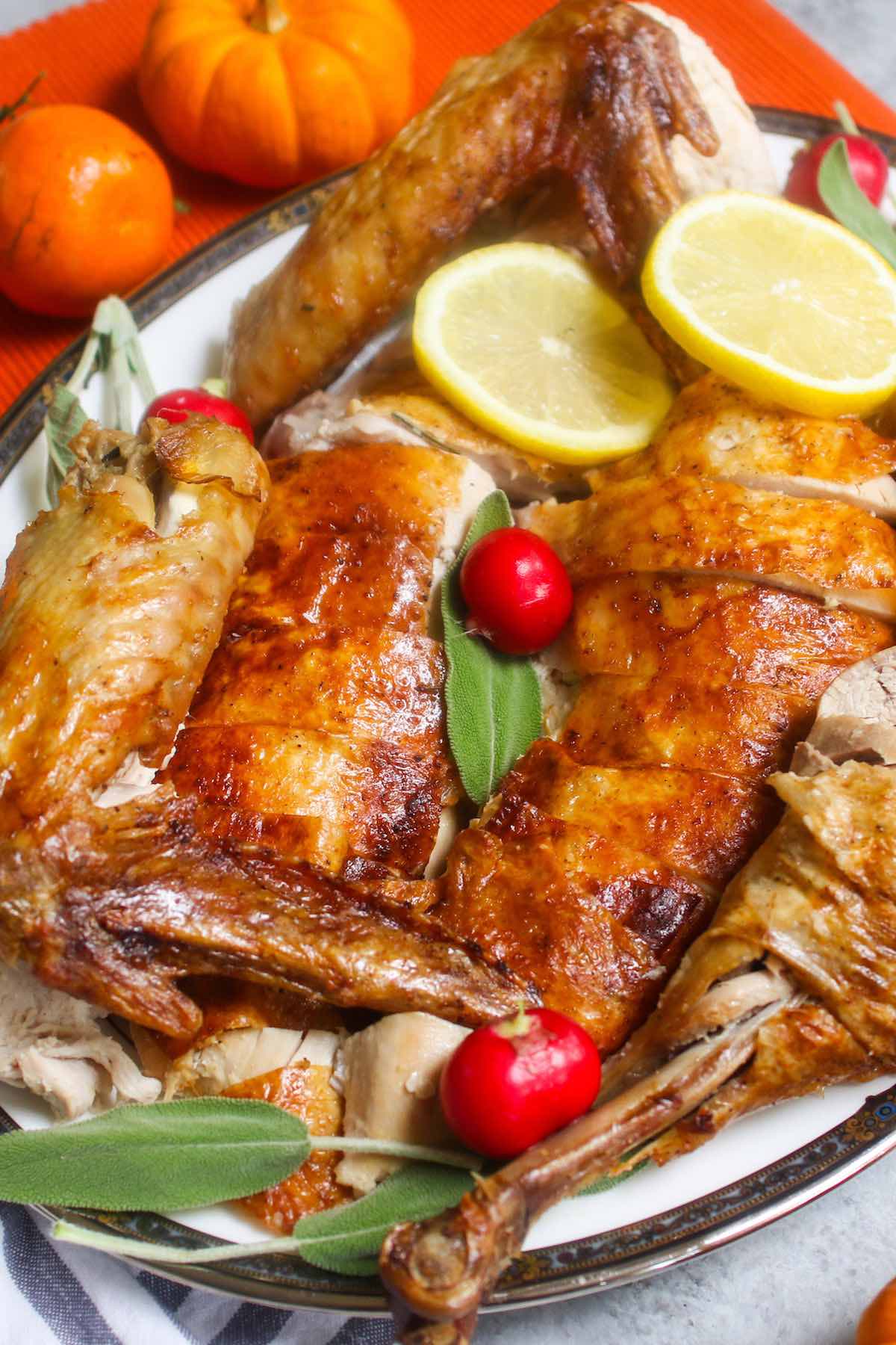 Carved roast turkey on a serving platter showing delicious golden wings, breasts, thighs and legs ready to eat with red radishes, lemon slices and fresh sage as garnishes