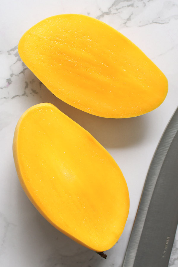 A ripe mango cut in half revealing deep yellow-orange flesh that's juicy and sweet