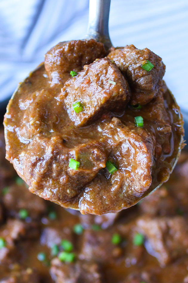 A ladle full of freshly made Mexican beef stew in a rich gravy, ready to be put into tortillas for a delicious meal.