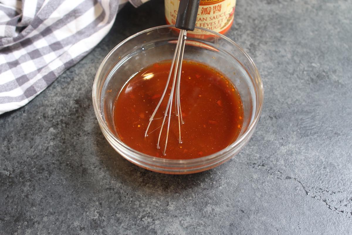 Making homemade Hunan sauce by whisking together chili bean paste, chicken broth, soy sauce, oyster sauce, vinegar, sugar, and cornstarch in a mixing bowl