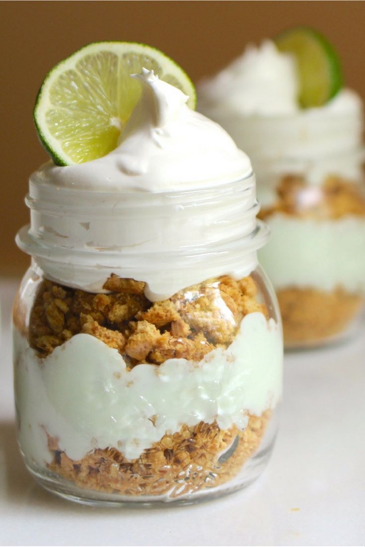 Closeup of key lime pie in a jar showing alternating layers of graham cracker crust and creamy filling with whipped cream and a lime wedge for garnish
