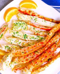 King crab legs served on a white plate with lemon wedges.