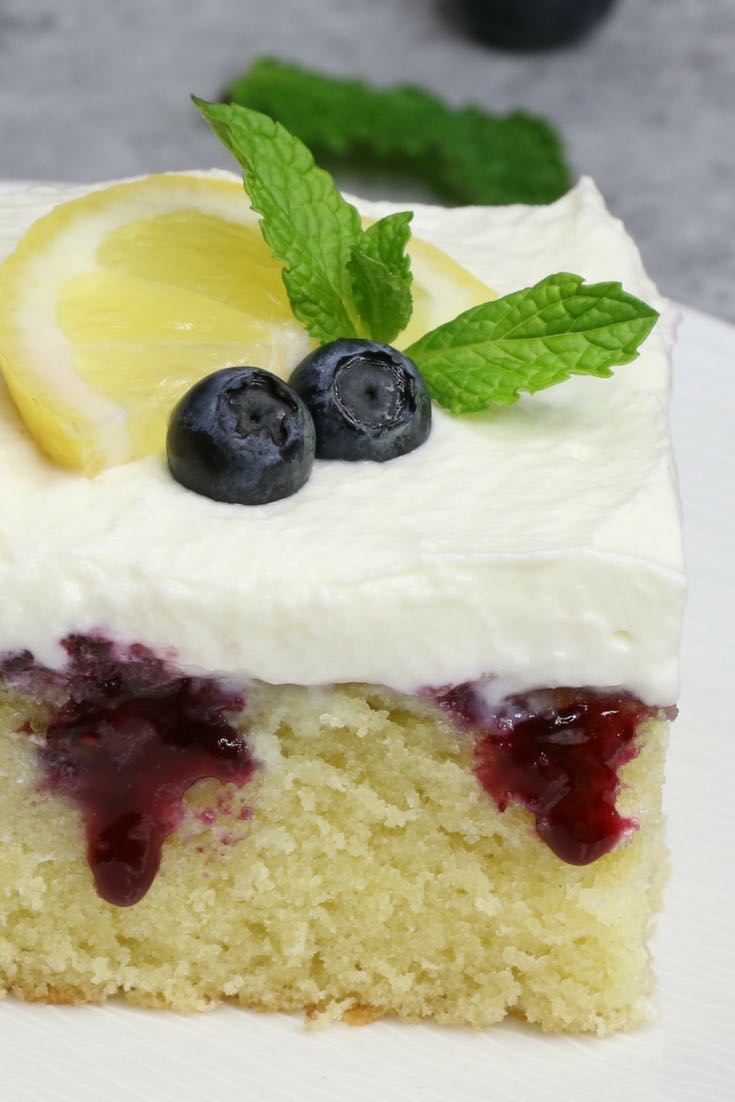 A serving of lemon blueberry poke cake garnished with fresh lemon and mint