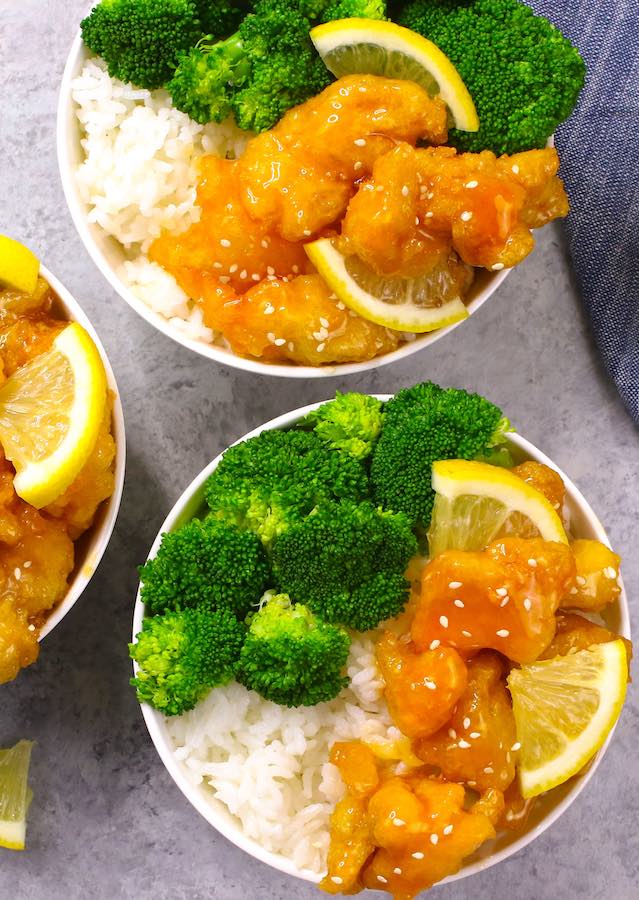 Chinese Lemon Chicken served in rice bowls with broccoli and garnished with sesame seeds and lemon wedges