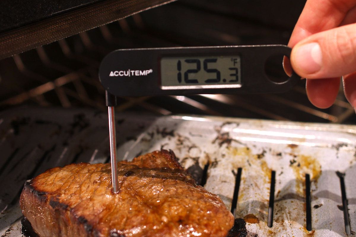 An instant-read thermometer inserted into the middle of a London Broil reading 125 degrees F indicating medium rare