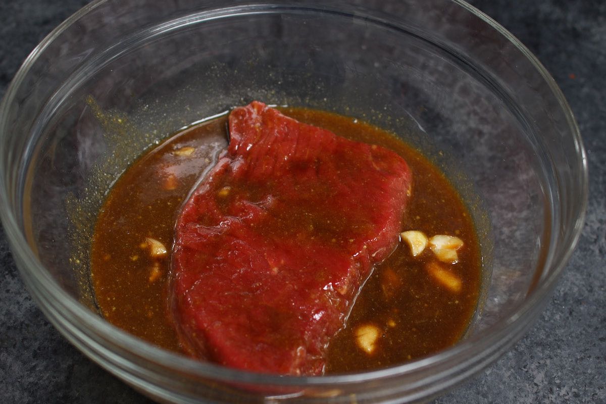 A piece of top round marinating in a bowl