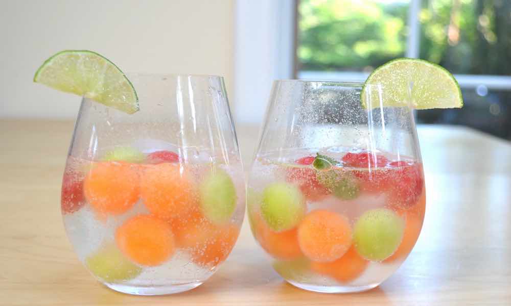 White sangria with melon balls served in stemless wine glasses and a twist of lime