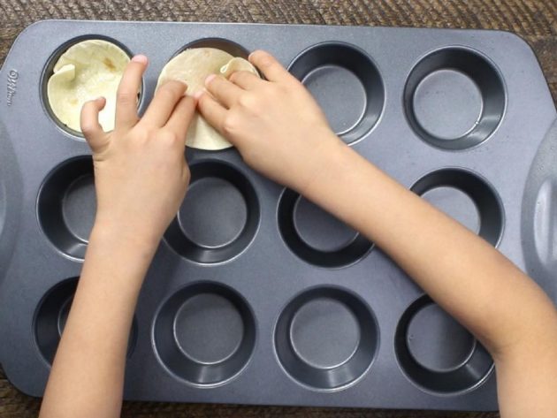 This is a process photo showing pressing tortilla cutouts into a muffin pan to bake
