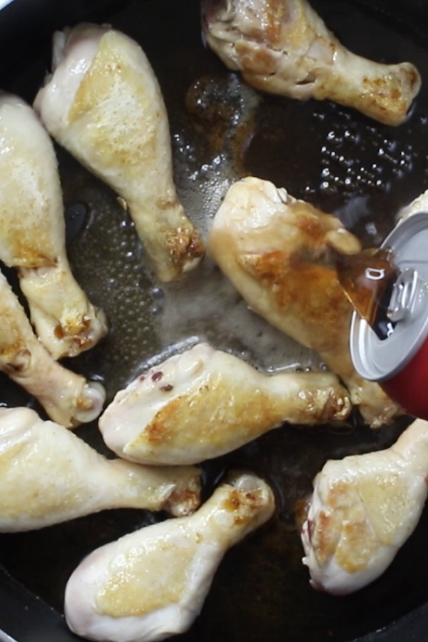 Overhead photo showing adding the coca cola to the skillet after browning the chicken pieces when making coca cola chicken