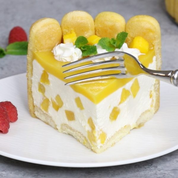 This photo shows a piece of Mango Charlotte Cake served on a plate with fresh raspberries and mint sprigs