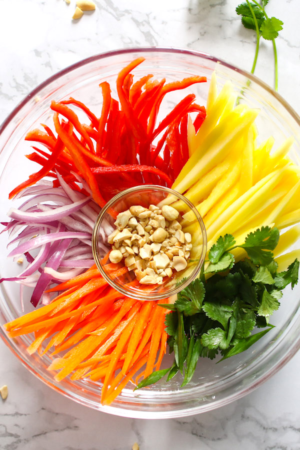The ingredients for mango salad arranged in a bowl: mango, bell pepper, carrots, cilantro, and red onions
