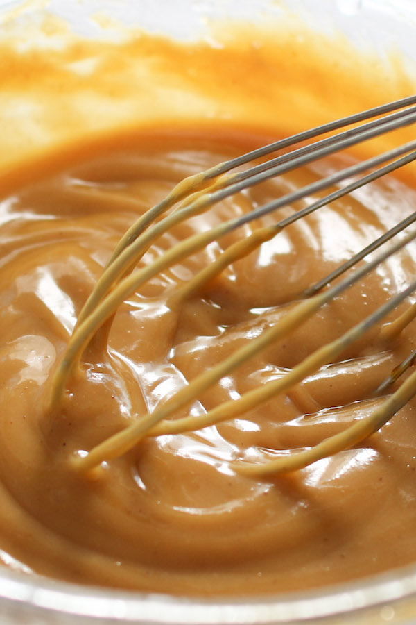 Closeup of whisking peanut dressing made with peanut butter, rice vinegar, honey, soy sauce, lime juice and oil in a mixing bowl