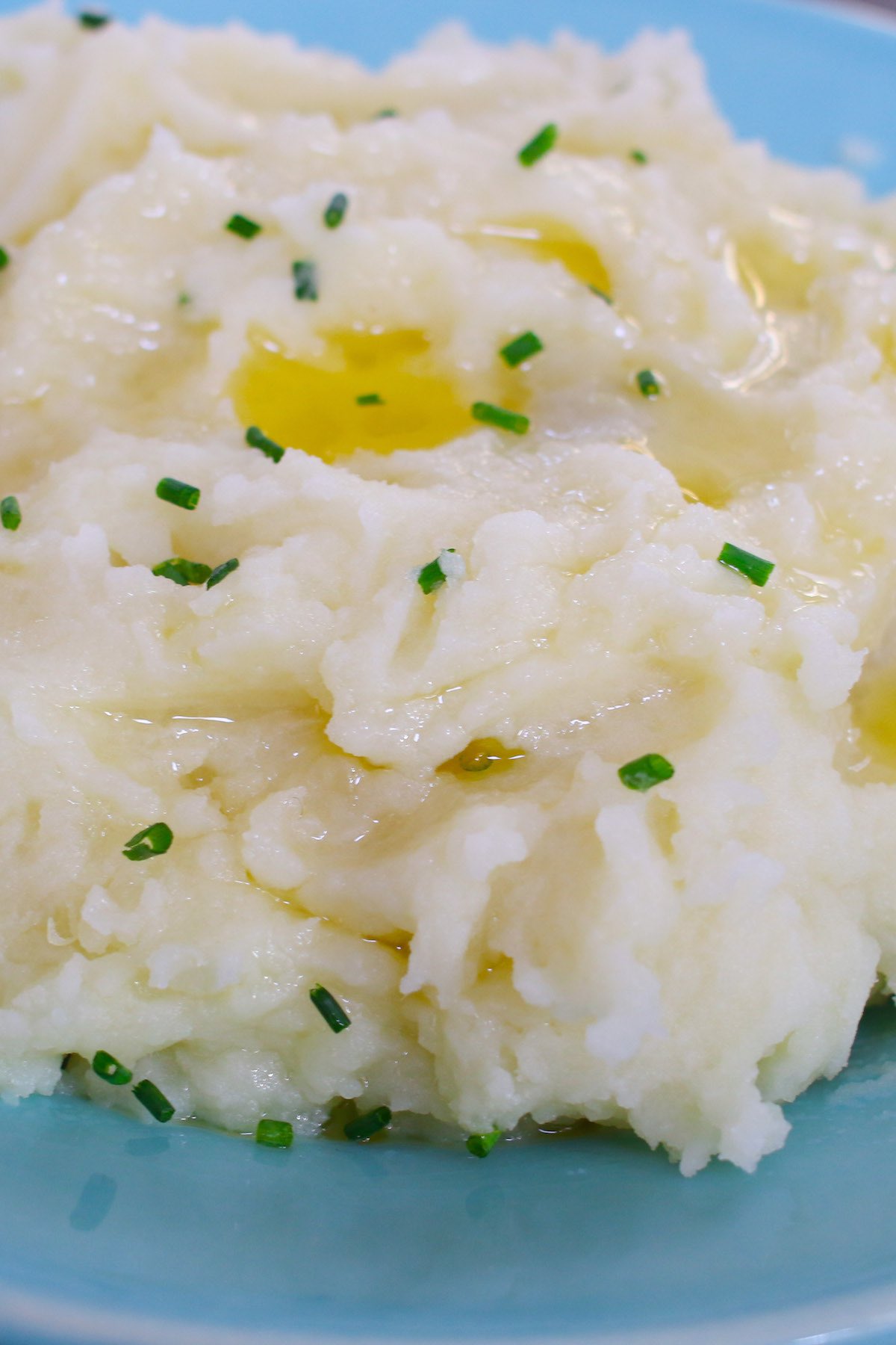 Microwave mashed potatoes garnished with chives and melted butter on a serving plate