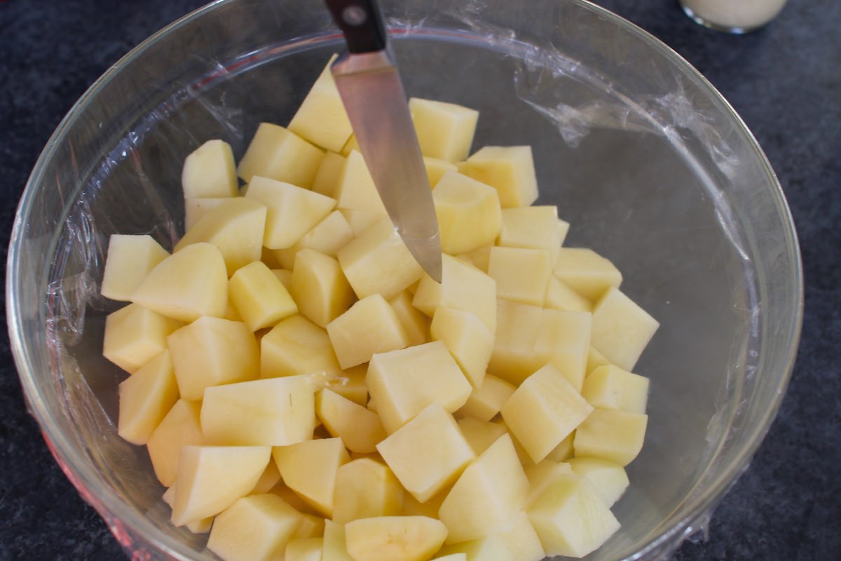 Poking a hole in the plastic wrap on a bowl of raw potato chunks to let steam escape during microwaving