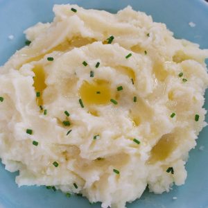 Microwave Mashed Potatoes on a serving plate garnished with fresh chives and melted butter for the perfect side dish