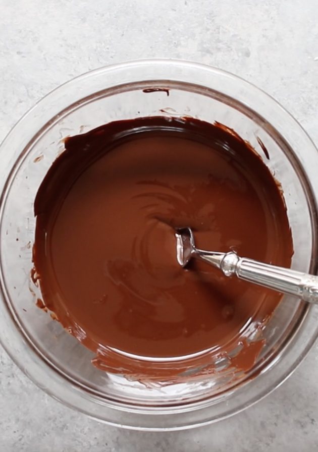 How to Melt Chocolate - this photo shows a mixing bowl full of melted dark chocolate and made smooth by stirring with a spoon.