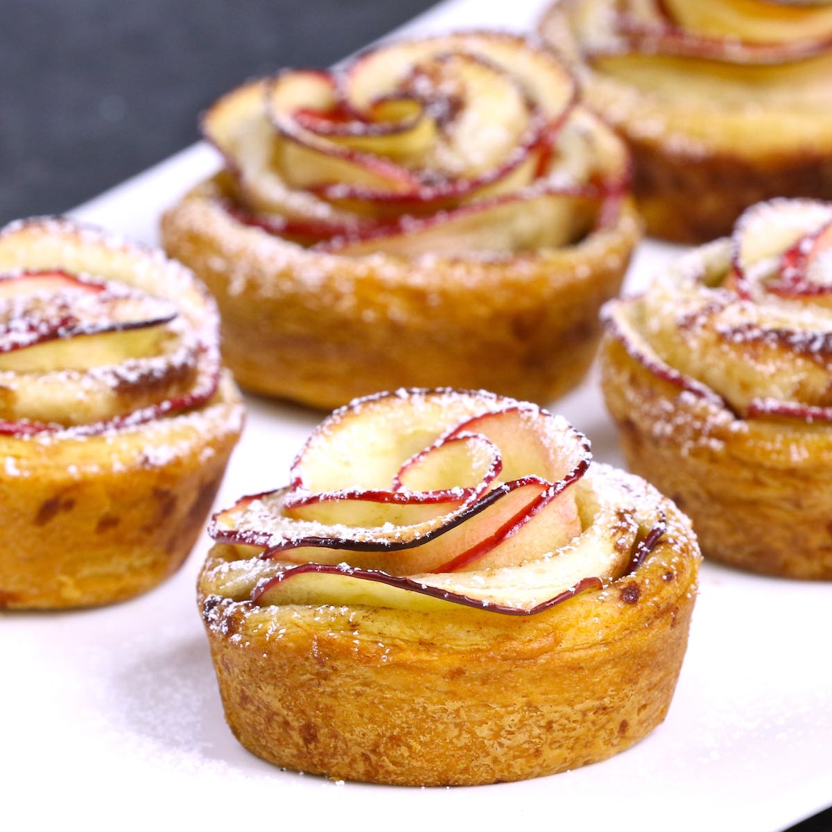 Apple rose tarts on a serving platter dusted with powdered sugar