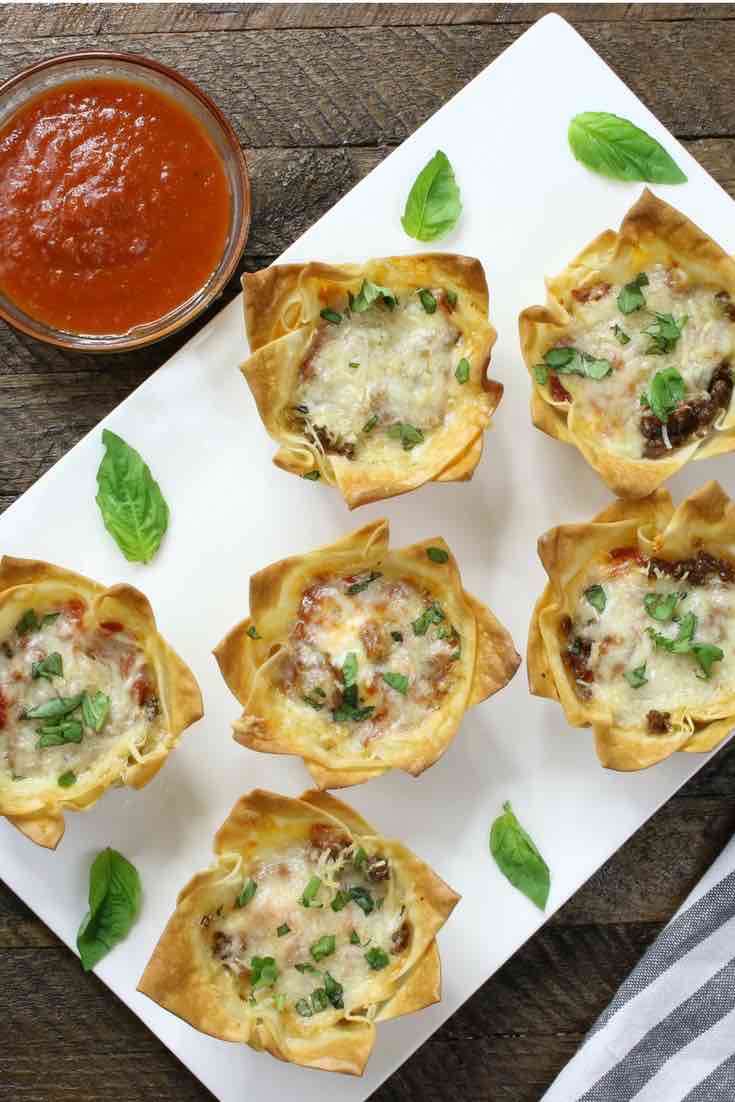 Overhead view of Mini Lasagna Cups on a serving plate garnished with fresh basil leaves and marinara sauce for dipping