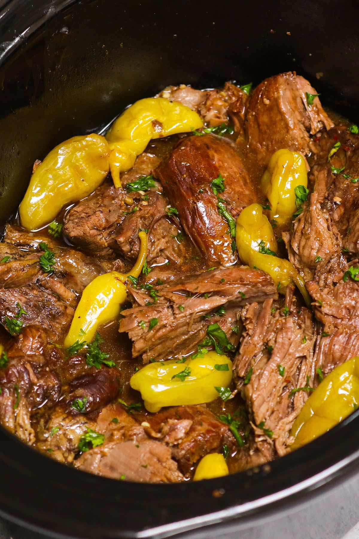 Closeup of Mississippi Pot Roast showing the deliciously tender chuck roast falling apart in the crockpot with juices and pepperoncini peppers.