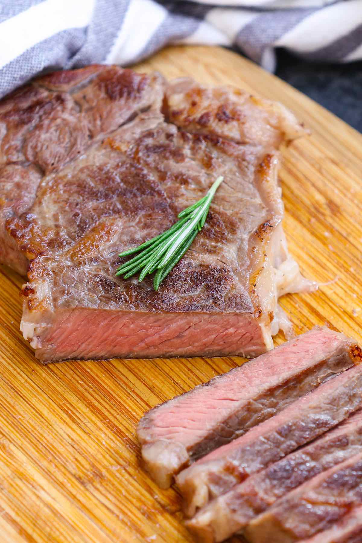 Sliced New York strip steak that has been pan seared to medium doneness and garnished with fresh rosemary