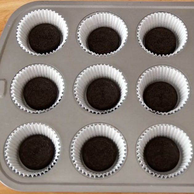 Mini Oreo Cheesecake Cupcakes - this photo show paper cupcakes cups in a muffin pan with an oreo placed in each as the first step in the recipe