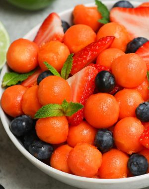 A bowl of freshly cut papaya with berries and mint sprigs