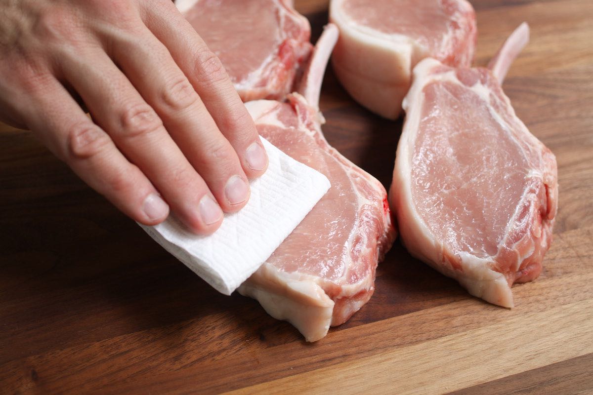 Patting dry pork chops with paper towels to remove excess moisture before cooking